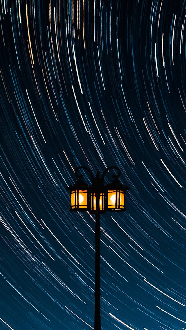 Stars whirling around the night sky behind a lamppost
